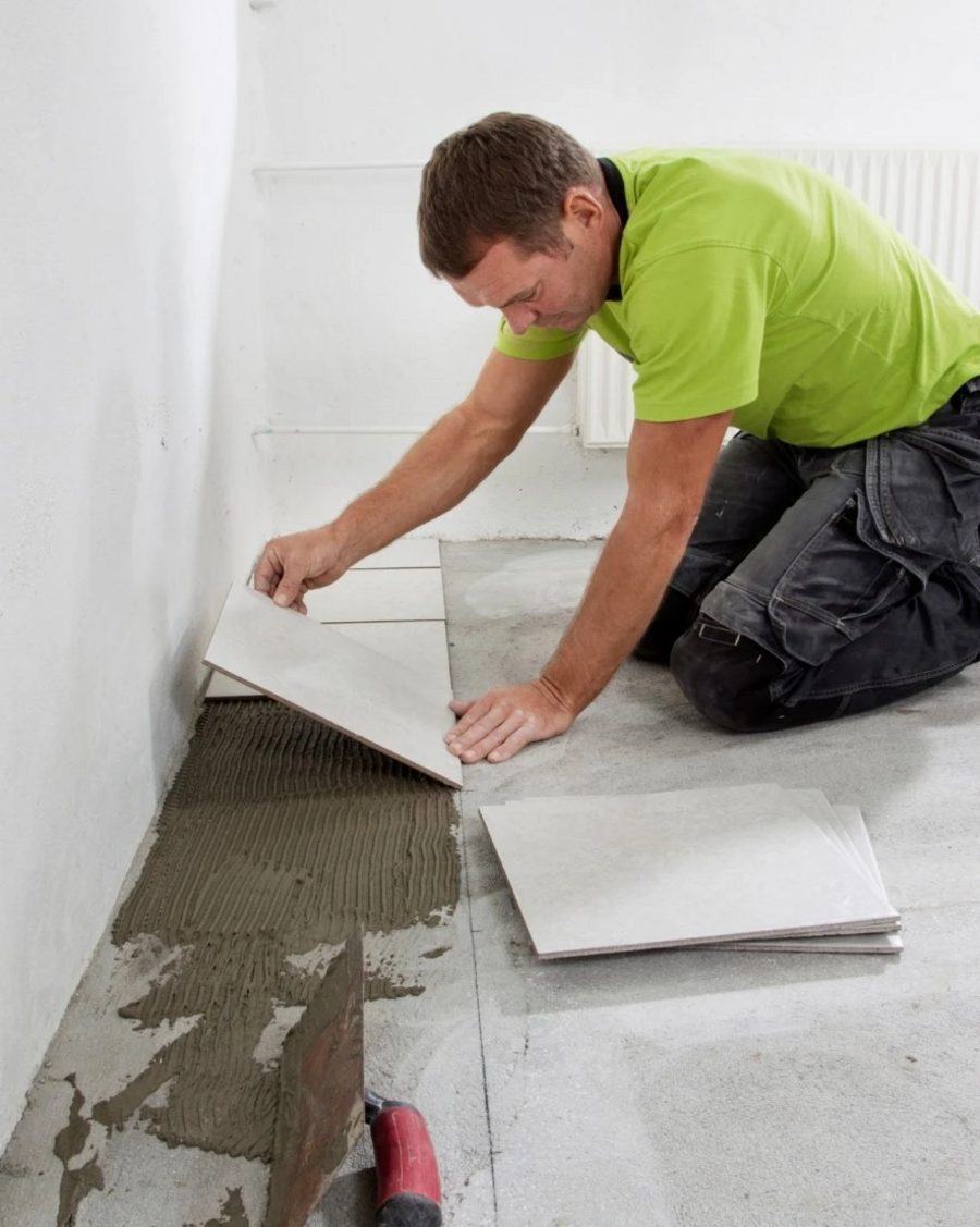 Tiler laying large-format floor tiles onto adhesive